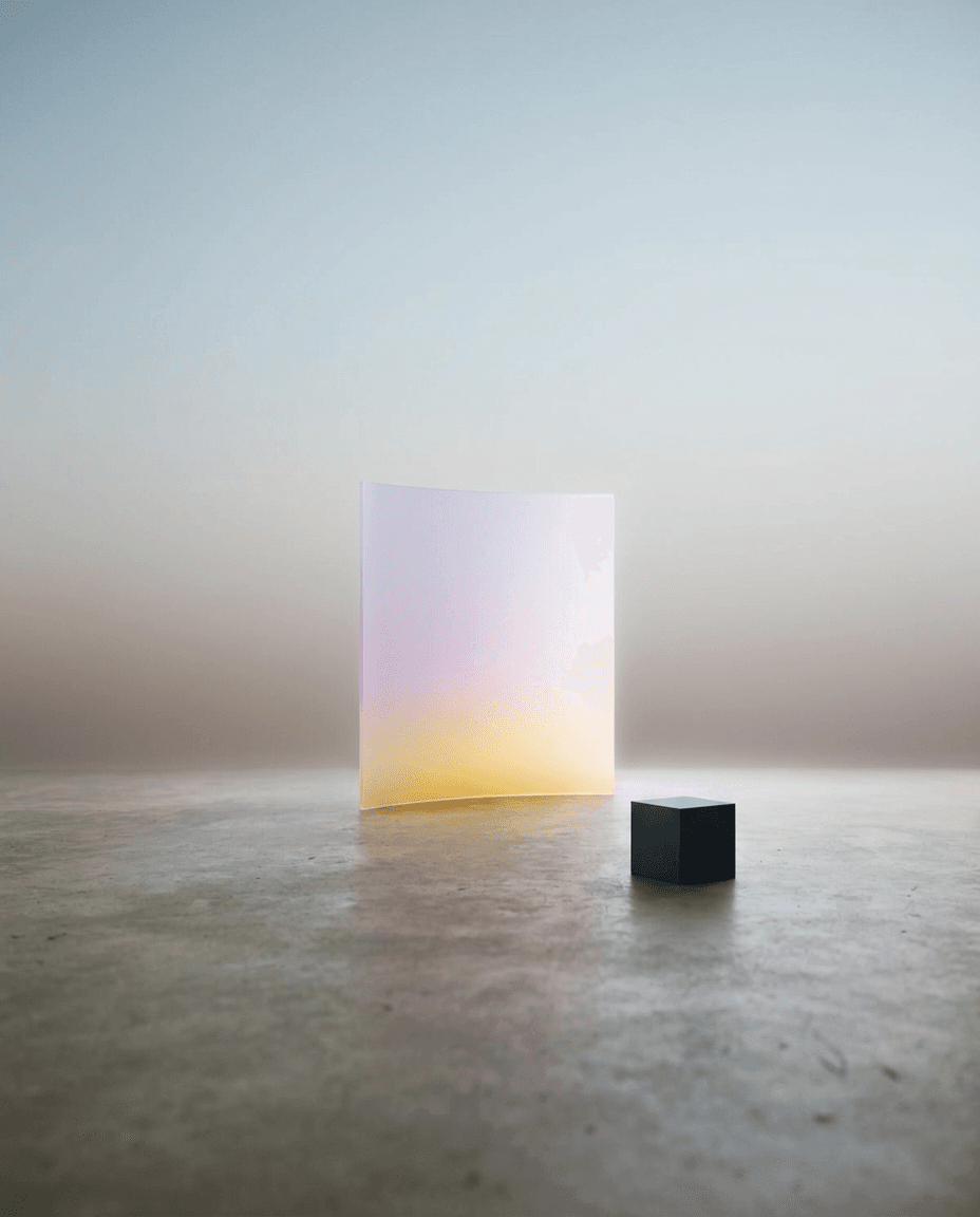 Still life with a translucent gradient panel in lilac and yellow next to a black cube.
