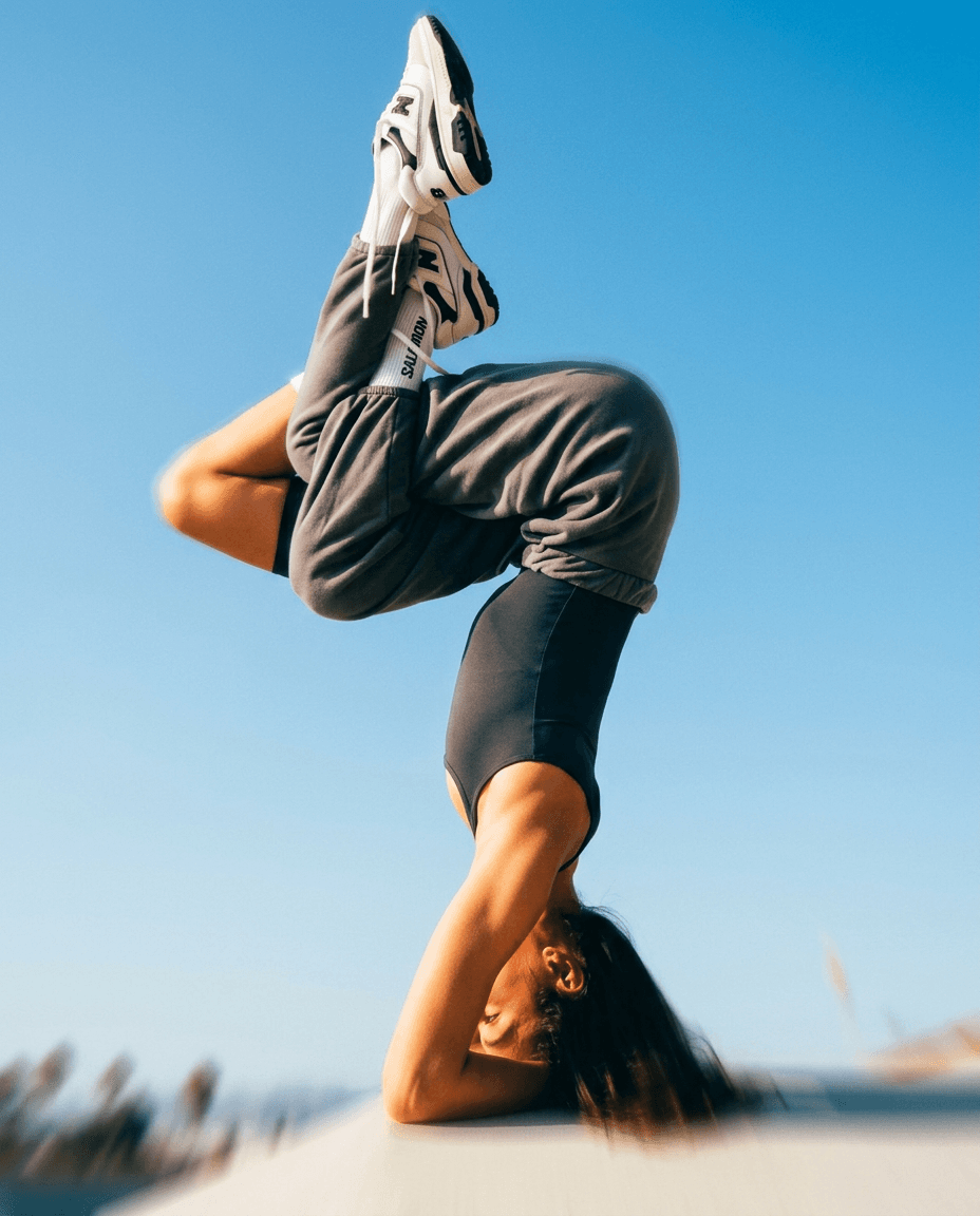 A woman in a headstand position against a clear blue sky.