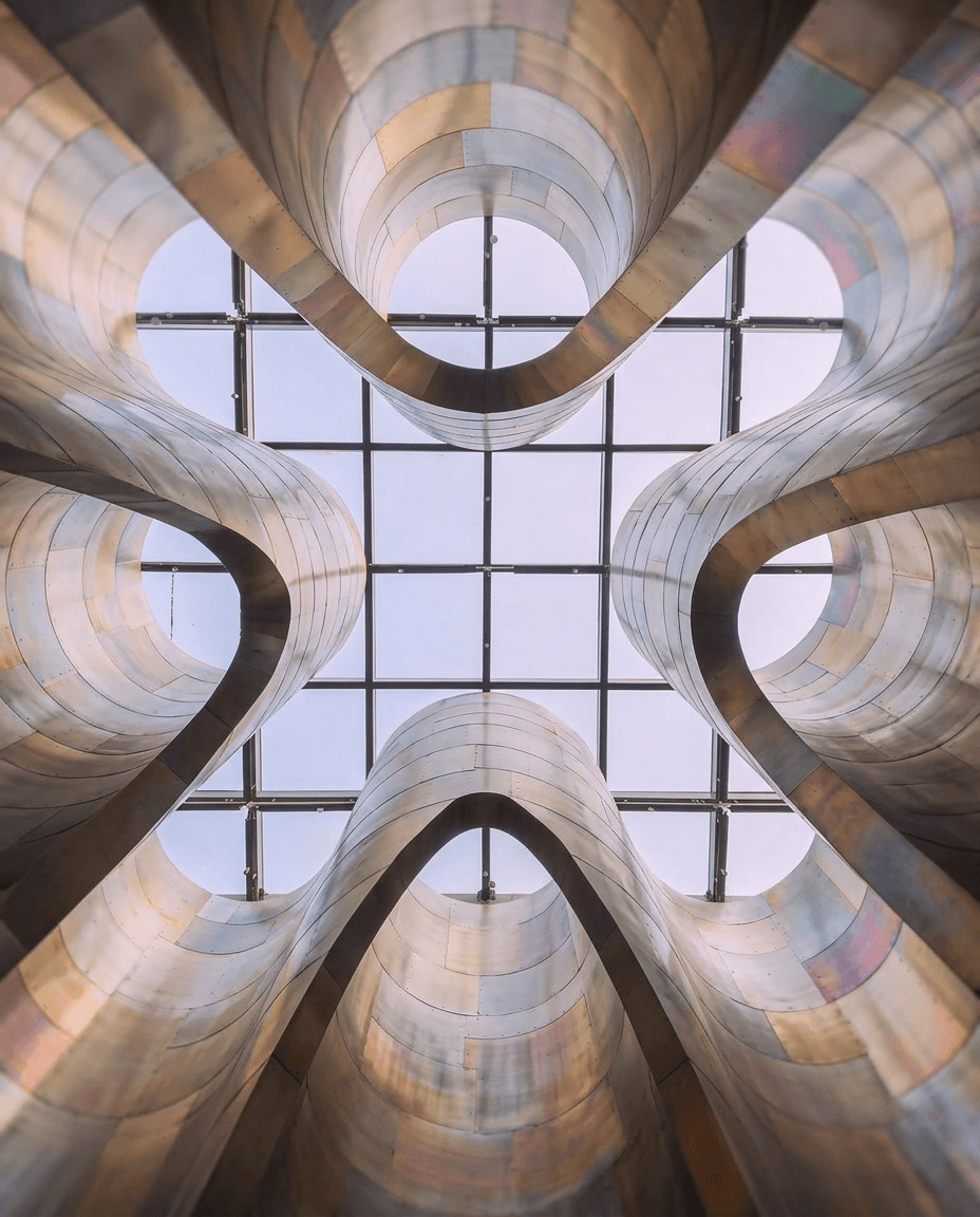 Curvilinear metallic structures converging towards a glass ceiling.