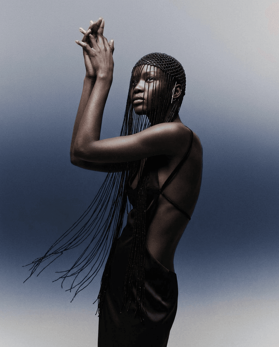 A model with braided hair poses against a gradient background from dark to light.