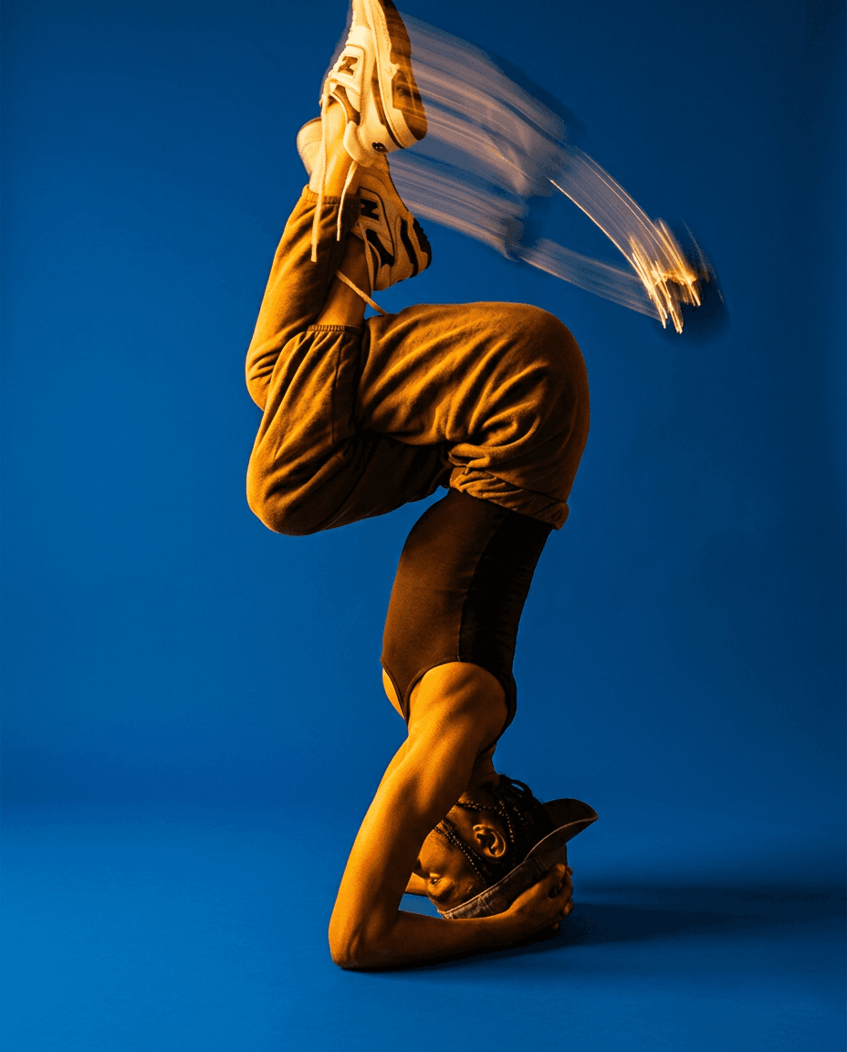 Dancer in headstand with blurred legs, vibrant blue background.