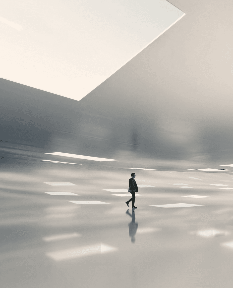 A solitary figure walking in a vast, softly lit minimalist space.