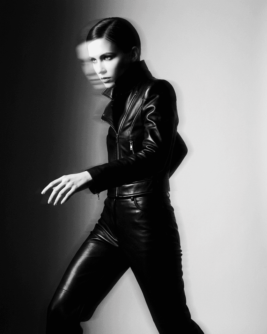 A model in a black leather outfit poses dynamically in high-contrast monochrome.