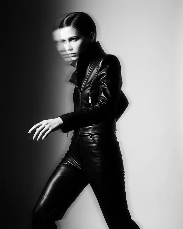 A model in a black leather outfit poses dynamically in high-contrast monochrome.
