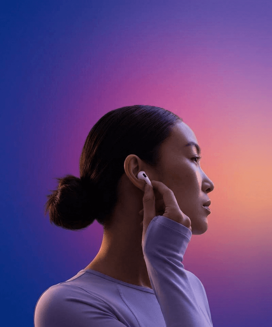 A woman in profile adjusting her earbud with a colourful gradient background.