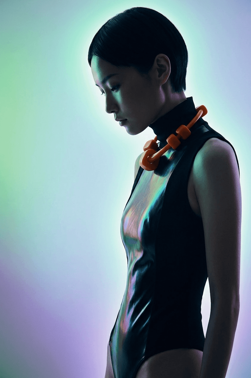 Young woman in a black bodysuit and orange necklace with a purple and green background.