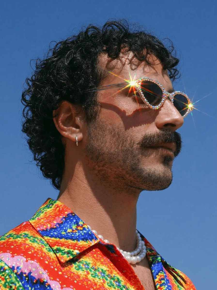 Portrait of a man in colourful clothing and reflective sunglasses under a blue sky.