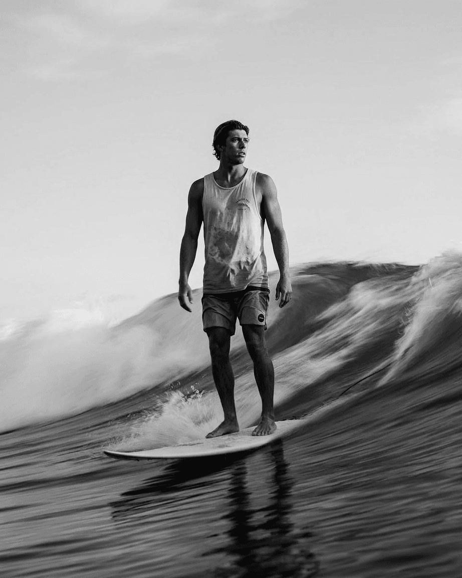 Black and white image of a male surfer riding a wave with contrasting shadows.