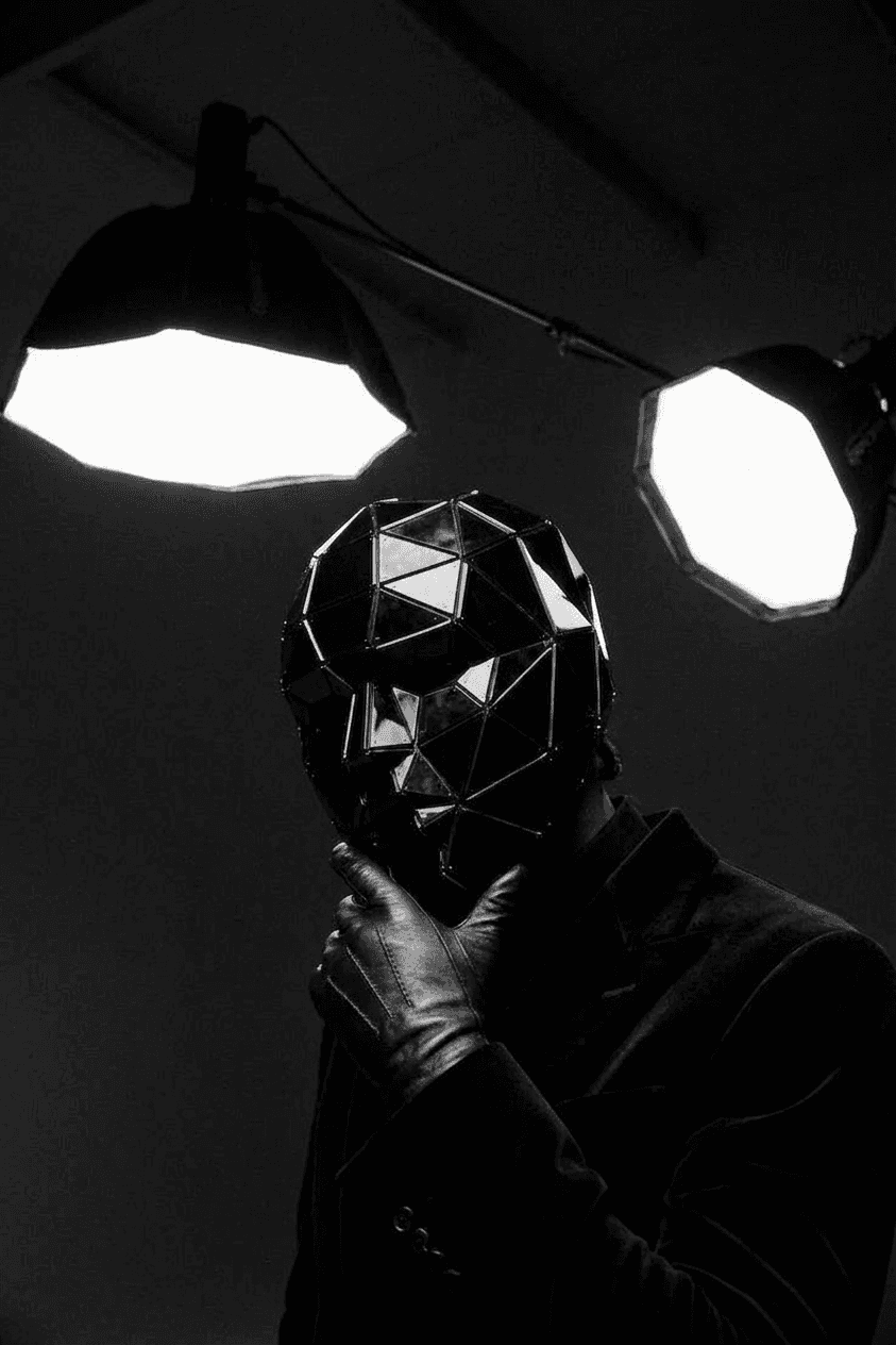 A figure wearing a geometric black mask poses under bright spotlights.