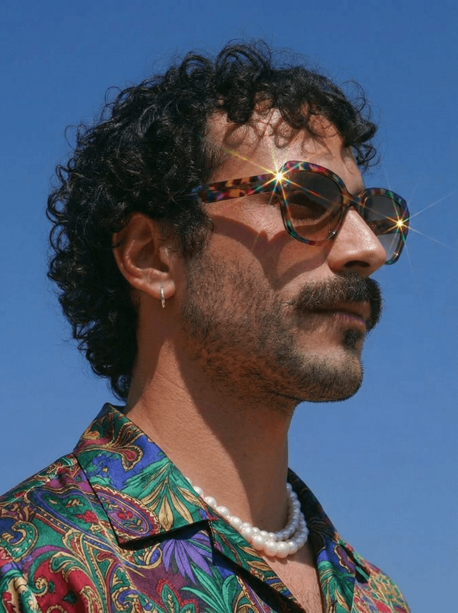 A stylish man poses confidently in front of a clear blue sky.