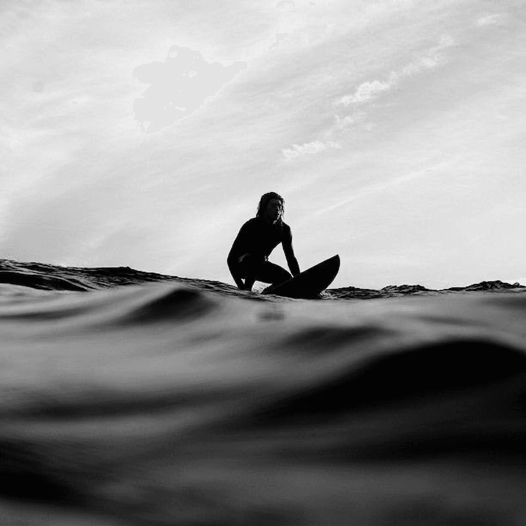 Black-and-white image of a lone surfer on a board in front of rolling waves.