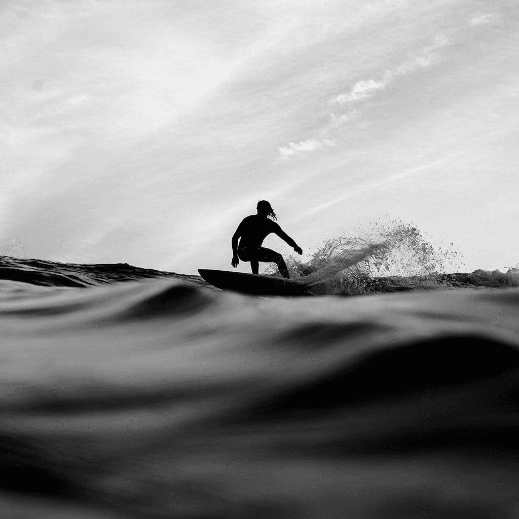 Black-and-white photo of a surfer navigating waves with deep shadows and grey tones.