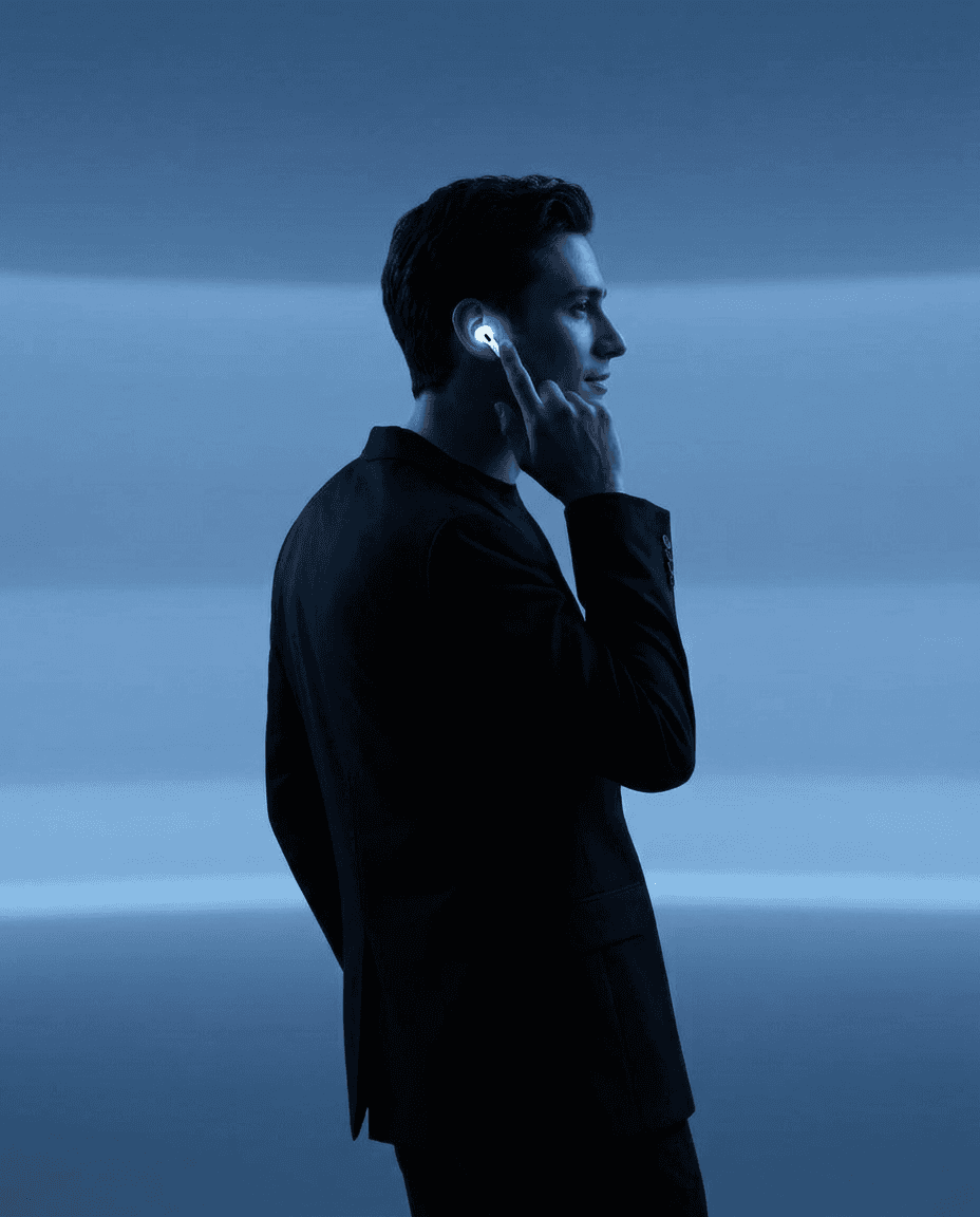 Portrait of a man in a suit with sleek hair, using wireless earbuds in soft blue lighting.