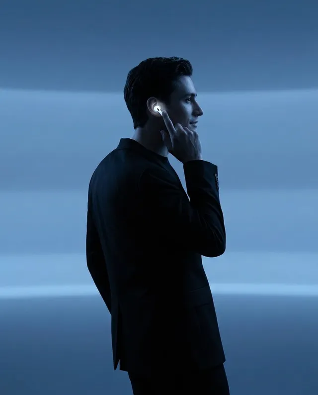 Portrait of a man in a suit with sleek hair, using wireless earbuds in soft blue lighting.