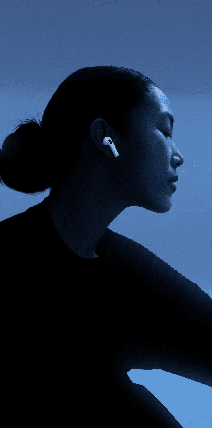 Profile of a woman with a sleek bun and wireless earbuds against a deep blue background.