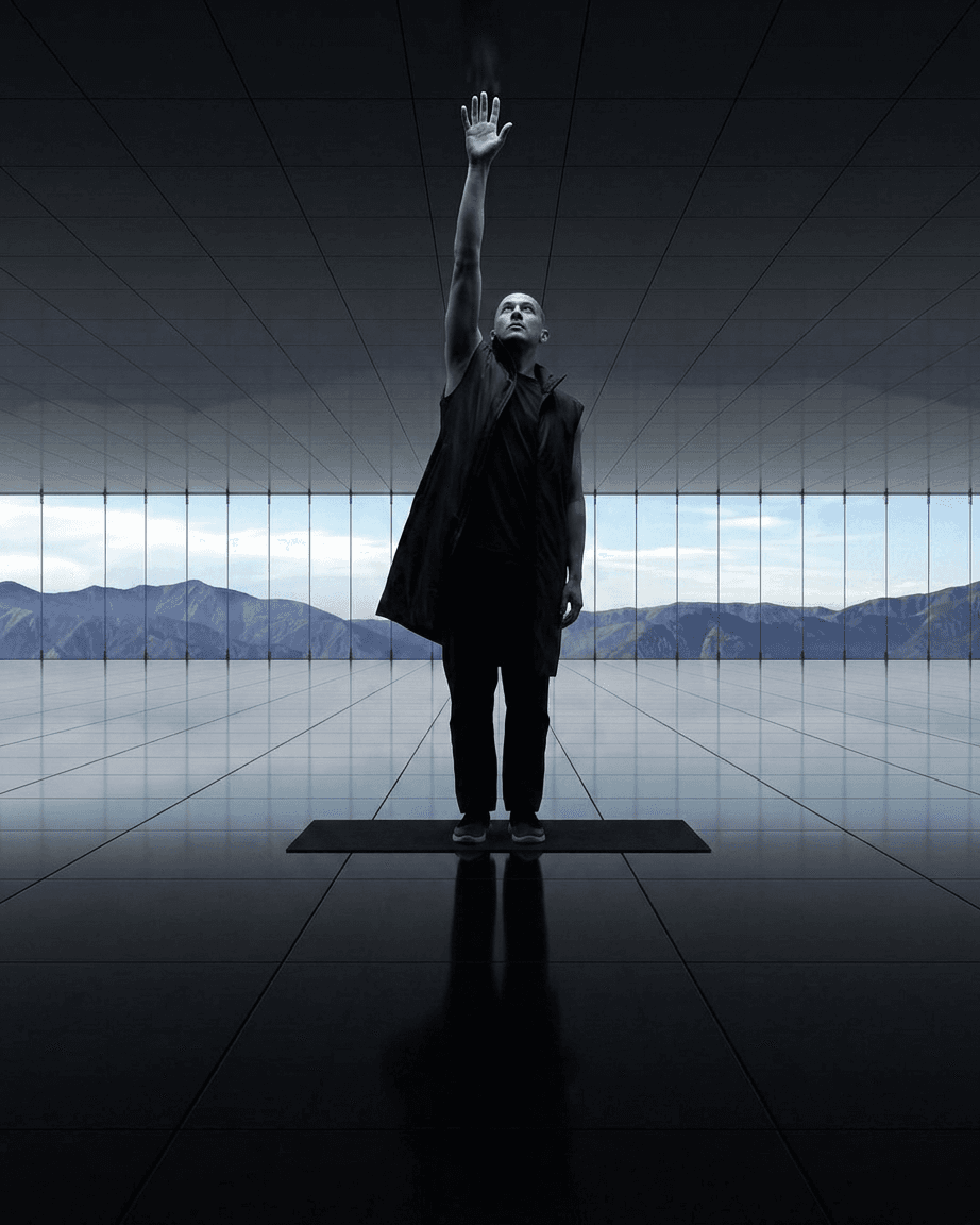 A person in black clothing stretches an arm in a sleek, reflective interior with mountain views.