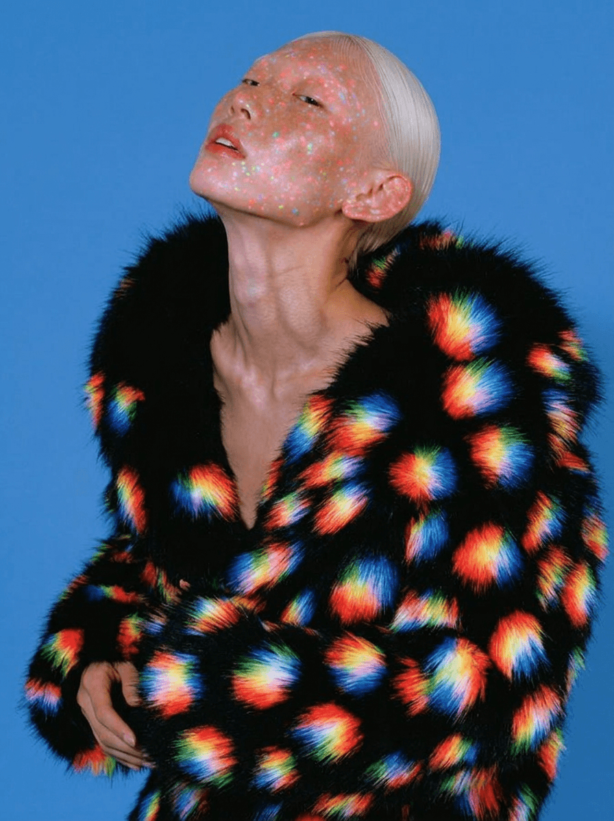 Model wearing a vibrant patterned fur coat against a bright blue background.