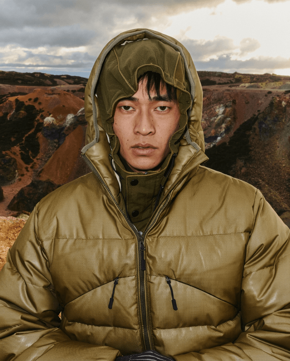 Close-up of a man in a greenish-brown puffer jacket in front of mountains.