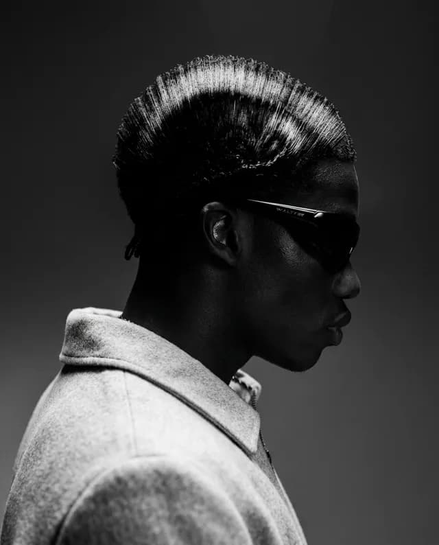 Profile of a stylish individual wearing sunglasses and a sleek hairstyle.