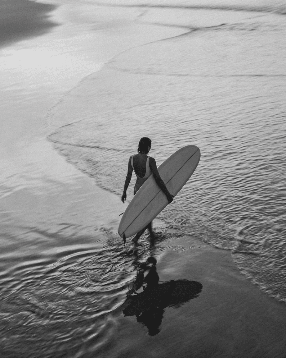 A woman wading through water at the shore, holding a surfboard.