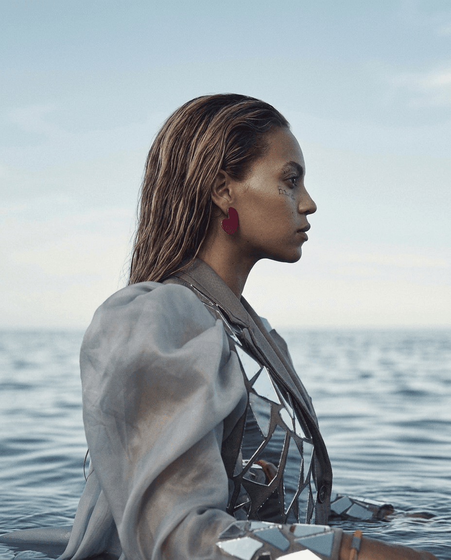 Woman with wet, wavy hair in a reflective outfit by the ocean.