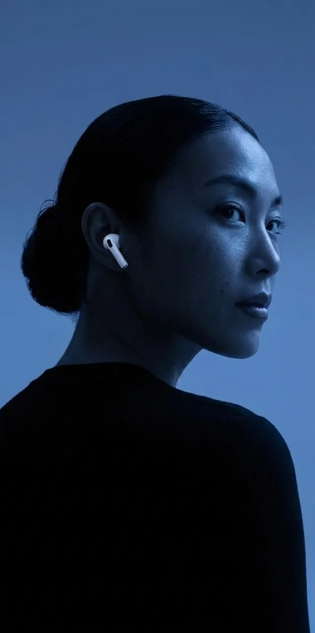 A woman with a sleek bun and white AirPods in a blue-toned setting.