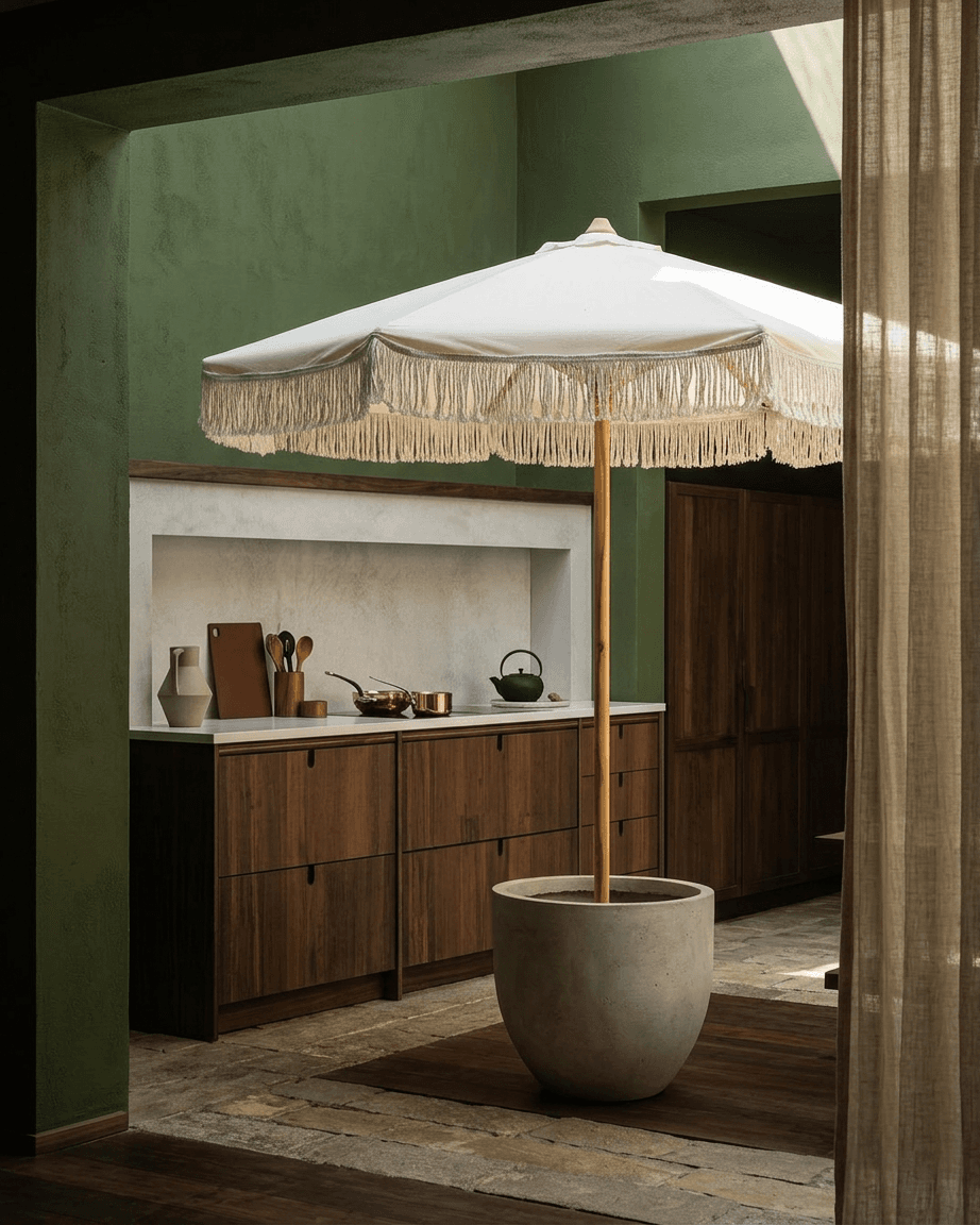 Indoor space with a large white fringed umbrella in a concrete pot and earthy green walls.