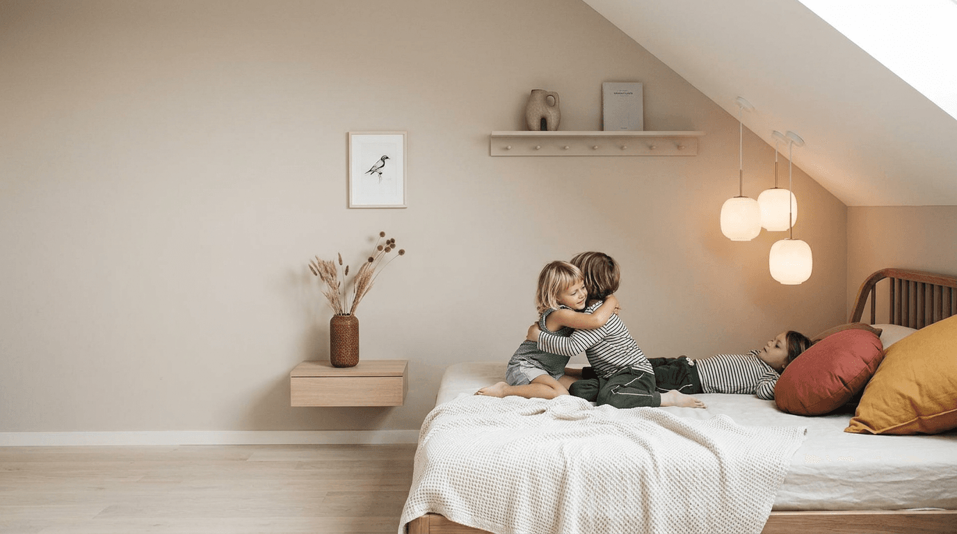 Three children hugging on a bed in a softly lit, minimalist bedroom.